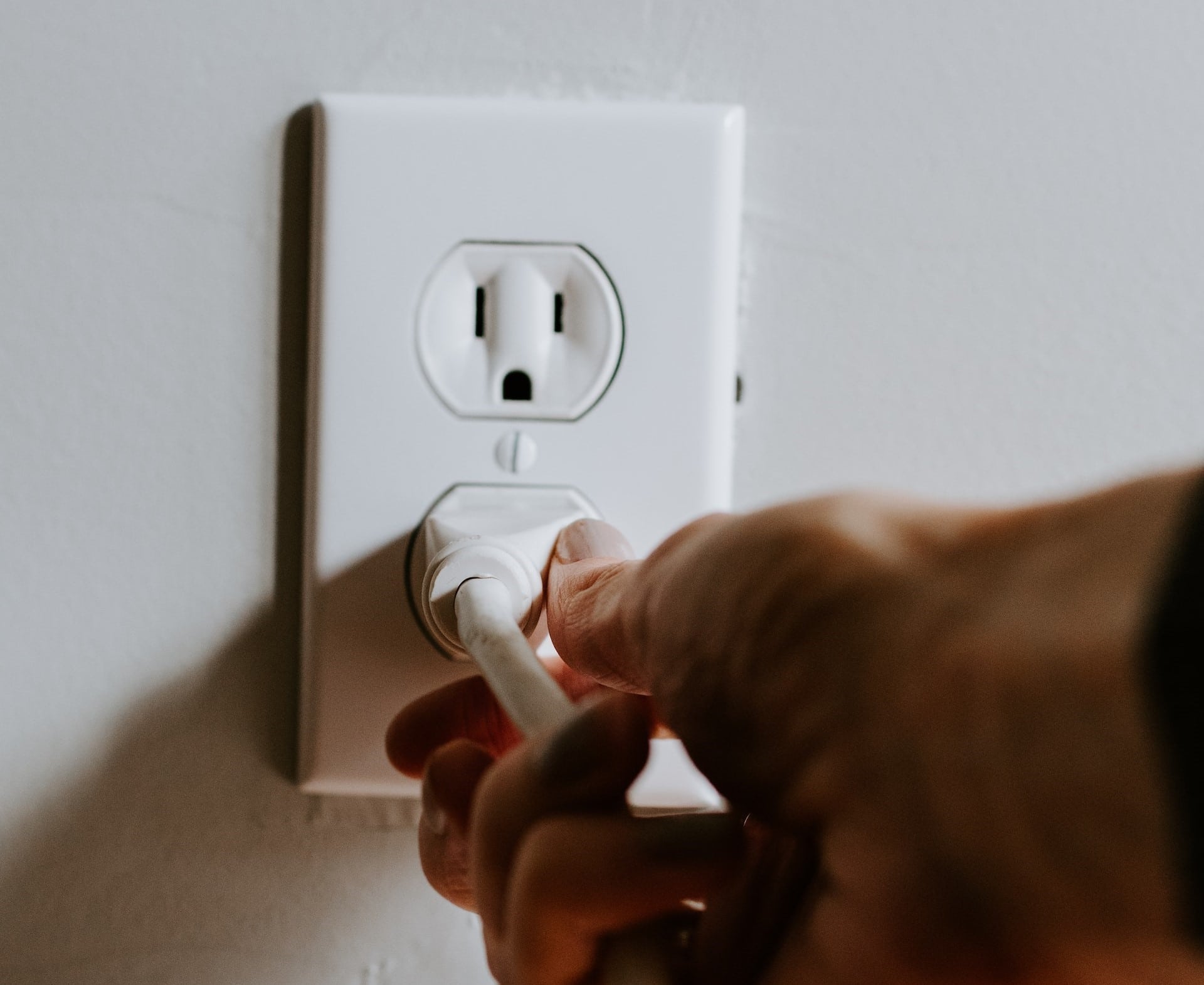 close-up of a hand plugging a cord into an electrical outlet in a home